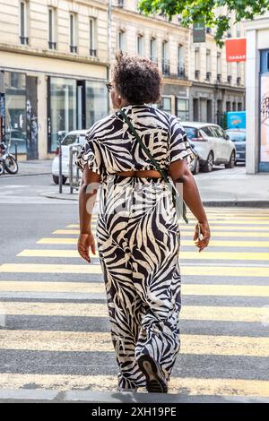 African woman in abstract black and white trouser suit dress crossing street - Paris 75004, France.trouser Stock Photo