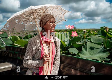 A woman wearing a hat and holding an umbrella is looking at a field of pink flowers. The scene is peaceful and serene, with the woman taking in the Stock Photo
