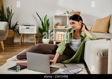 Stylish woman in casual attire sitting on floor, focused on laptop work. Stock Photo