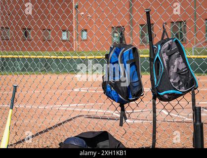 Baseball backpacks hanging on chain link fence at little league baseball field Stock Photo