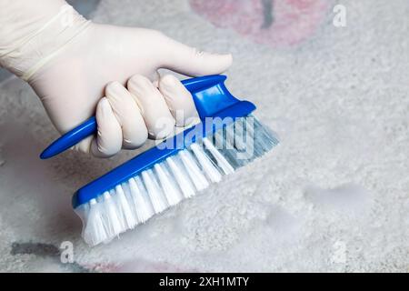 Hand in rubber glove holding the brush for cleaning. Plastic blue brush and foam for cleaning on the floor. Stock Photo