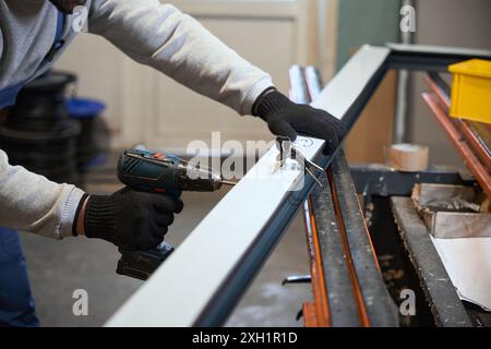 Worker in protective gloves uses drill while working with window profile Stock Photo