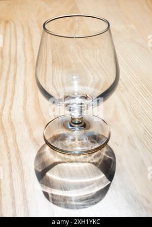 Empty wine or shot glass seen from above in backlight with shadow on wooden background. Focus on the base of the glass Stock Photo