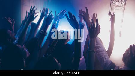 Cheering live shine show performance concept. Crowd shadow of people at during a concert dancing in party club with neon lights raised hands up Stock Photo