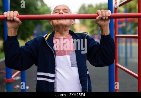 Sportive old man doing pull-ups outdoors Stock Photo