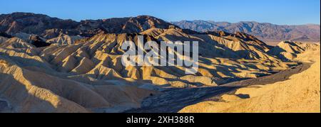 Sunrise at Golden Desert Valley - Panorama overview of soft morning sunlight shining on colorful rolling mud stone hills at Zabriskie Point. CA, USA. Stock Photo