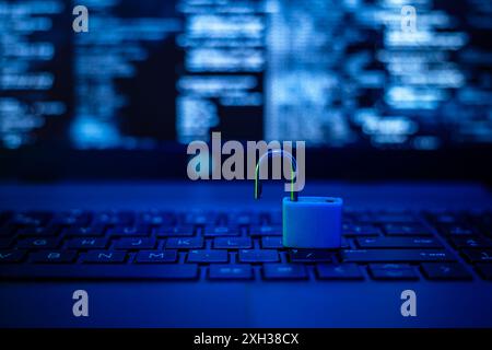 A blue padlock sits open on the keyboard of a laptop, with a blurred background of code. Stock Photo