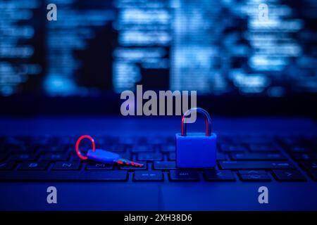 A blue padlock sits on a laptop keyboard, with a red key lying next to it. The keyboard is illuminated in blue light, with a blurred screen displaying Stock Photo