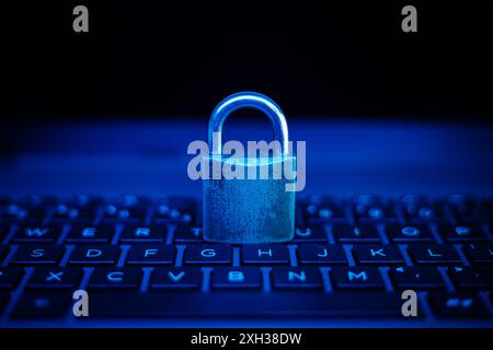 A metal padlock sits on a blue lit laptop keyboard, symbolizing online security. Stock Photo