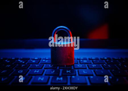A closed metal padlock sits on a laptop keyboard illuminated by blue and red light. Stock Photo