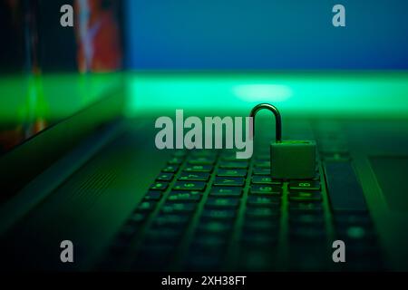 A silver padlock sits open on a laptop keyboard, illuminated by a green light. Stock Photo
