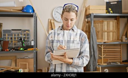 A focused woman taking notes in a well-organized workshop. Stock Photo
