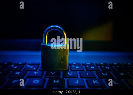 A metal padlock sits on a laptop keyboard illuminated with blue and yellow light. Stock Photo