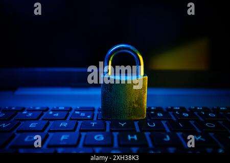 A metal padlock sits on a laptop keyboard, illuminated by blue and yellow light. Stock Photo