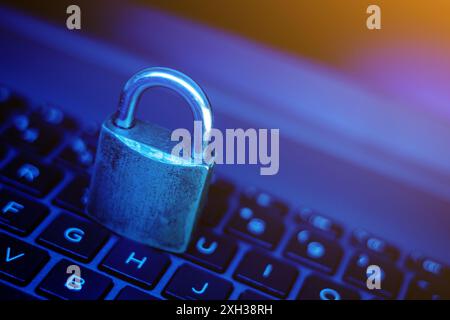 A metal padlock rests on the keys of a laptop keyboard. The image is lit with blue light. Stock Photo
