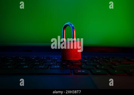 A red padlock sits on a laptop keyboard in front of a green screen. Stock Photo