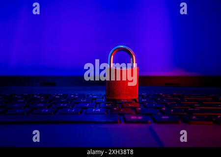 A red padlock sits on a laptop keyboard, illuminated by blue and red light. Stock Photo