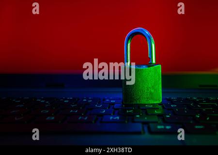 A metal padlock sits on a laptop keyboard, illuminated by red and blue lights. Stock Photo