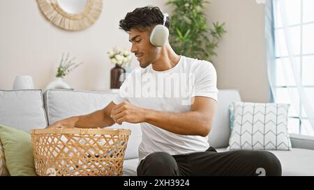 Handsome hispanic man listening to music on headphones while doing laundry at home Stock Photo