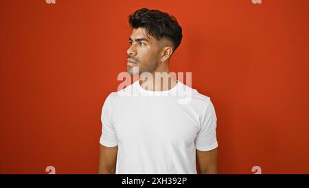 A handsome young hispanic man with a beard poses confidently against an isolated red background. Stock Photo