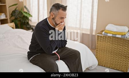 Mature hispanic man with gray beard feeling sick in bedroom Stock Photo