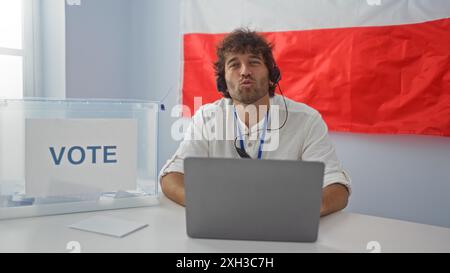 Young man indoors at a voting station with polish flag working on laptop wearing headset Stock Photo