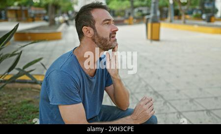 Thoughtful bearded man in blue shirt sitting outdoors in a city park. Stock Photo