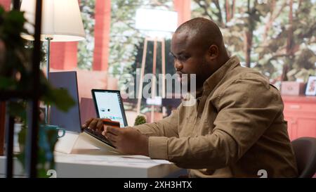 Business owner makes a payment with his card for online shopping at his home, electronic banking to buy resources for his startup. Entrepreneur purchasing something on laptop. Camera A. Stock Photo