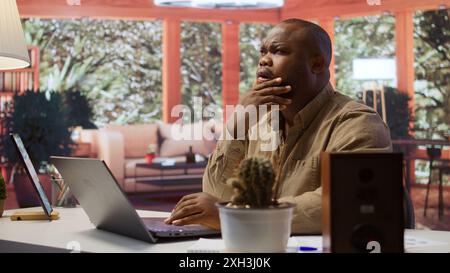 Freelancer managing startup projects and thinking about client needs from his home office, developing new growth strategy. Self employed analyst does telecommuting work on laptop. Camera B. Stock Photo