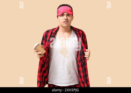 Stressed young man with coffee stains on his pajamas on beige background Stock Photo