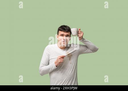 Stressed young man with coffee stains on his t-shirt on green background Stock Photo