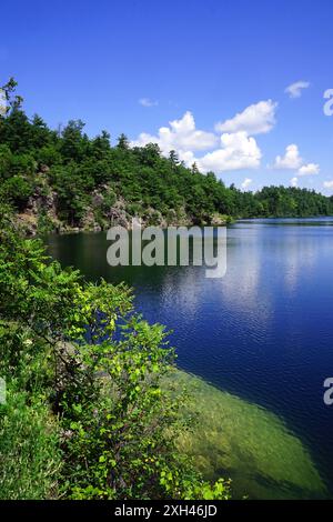 Thick forest and rocky cliffs above a lake on a summer afternoon in Gatineau Park Stock Photo