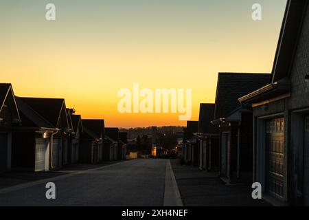 Sunset sky above suburban street - row of houses with prominent garages - warm golden hour light casting long shadows - clear, cloudless horizon - tra Stock Photo