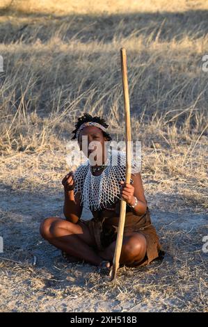 A female San bushmen, adorned with beadwork, sitting cross legged on ...