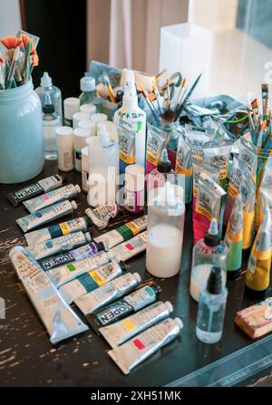 A detailed shot of an artist's workspace featuring various paints, brushes, and art supplies arranged neatly on a table. Stock Photo