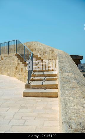 Stone staircase with a metal railing leading up to a historic stone wall, set against a clear blue sky. Architecture and heritage. Stock Photo