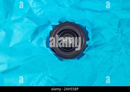 Camera lens taking pictures thru a torn hole in blue crumpled paper, soft focus Stock Photo