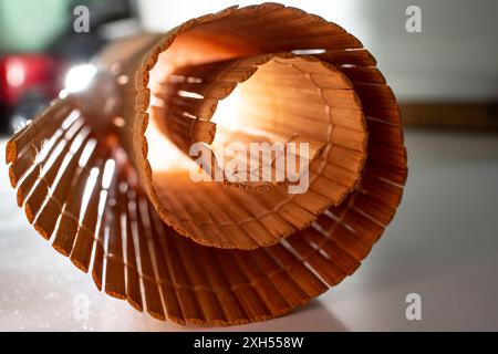 A close up of a side of a rolled up woven bamboo sushi rolling mat placed on the corner edge of a wooden table perspective spiral backlit Stock Photo