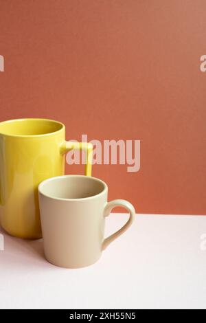 Yellow and beige mug cups on pink table. red background Stock Photo