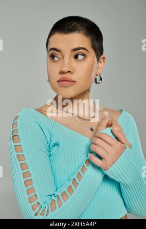 A young woman with short hair, dressed in a blue top, striking a pose against a grey background. Stock Photo