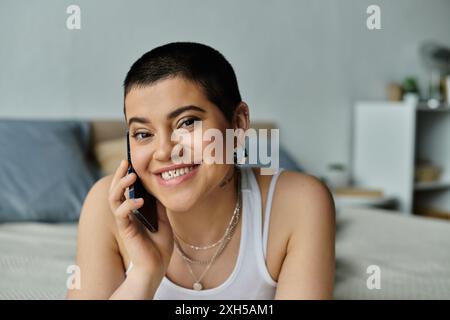 Young woman in casual wear, sitting on bed, talking on cell phone. Stock Photo