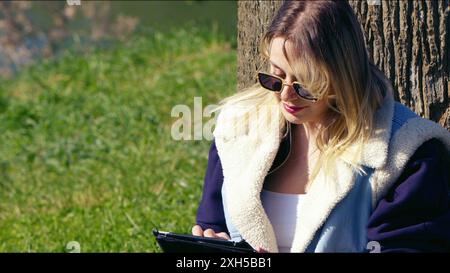 A Young Blond Woman is Working on Electronic Tablet PC in Nature Stock Photo