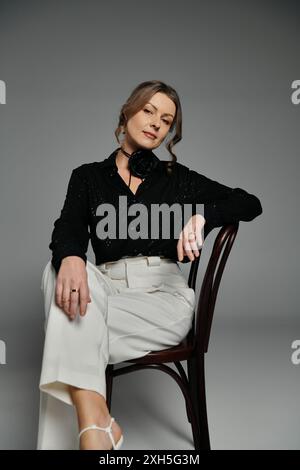 A woman in a black blouse and white pants poses while sitting on a chair. Stock Photo