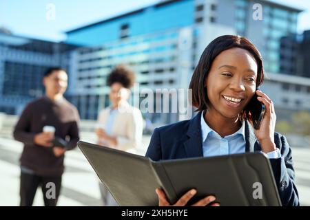 Smiling Businesswoman Talking on Phone in Urban Setting with Diverse Business Group Stock Photo