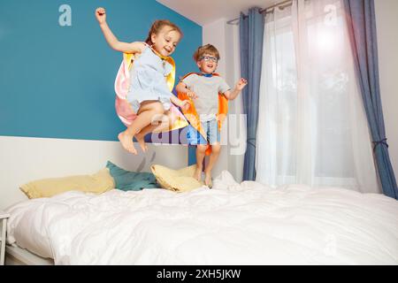 Children in vibrant superhero capes happily springing on a bed Stock Photo