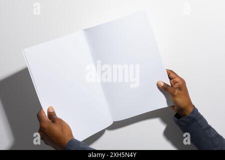Hands of an African American man holding an open blank magazine, with copy space. Ideal for showcasing design work or print layout in a professional s Stock Photo