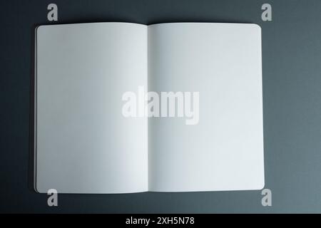 An open blank notebook lies on a dark surface, with copy space. Ideal for adding text or graphics, the notebook offers a clean slate for creativity or Stock Photo