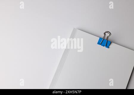 A blue paper clip on white sheets, with copy space. Essential office supplies captured in a minimalist setting emphasize organization. Stock Photo