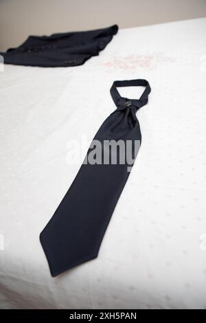 Elegant blue tie lying on a bed with a business suit jacket in the background Stock Photo