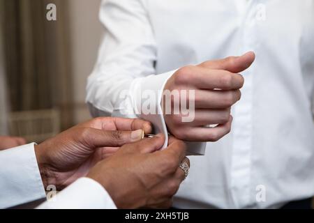Best man is helping groom getting ready for wedding ceremony by attaching cufflinks Stock Photo